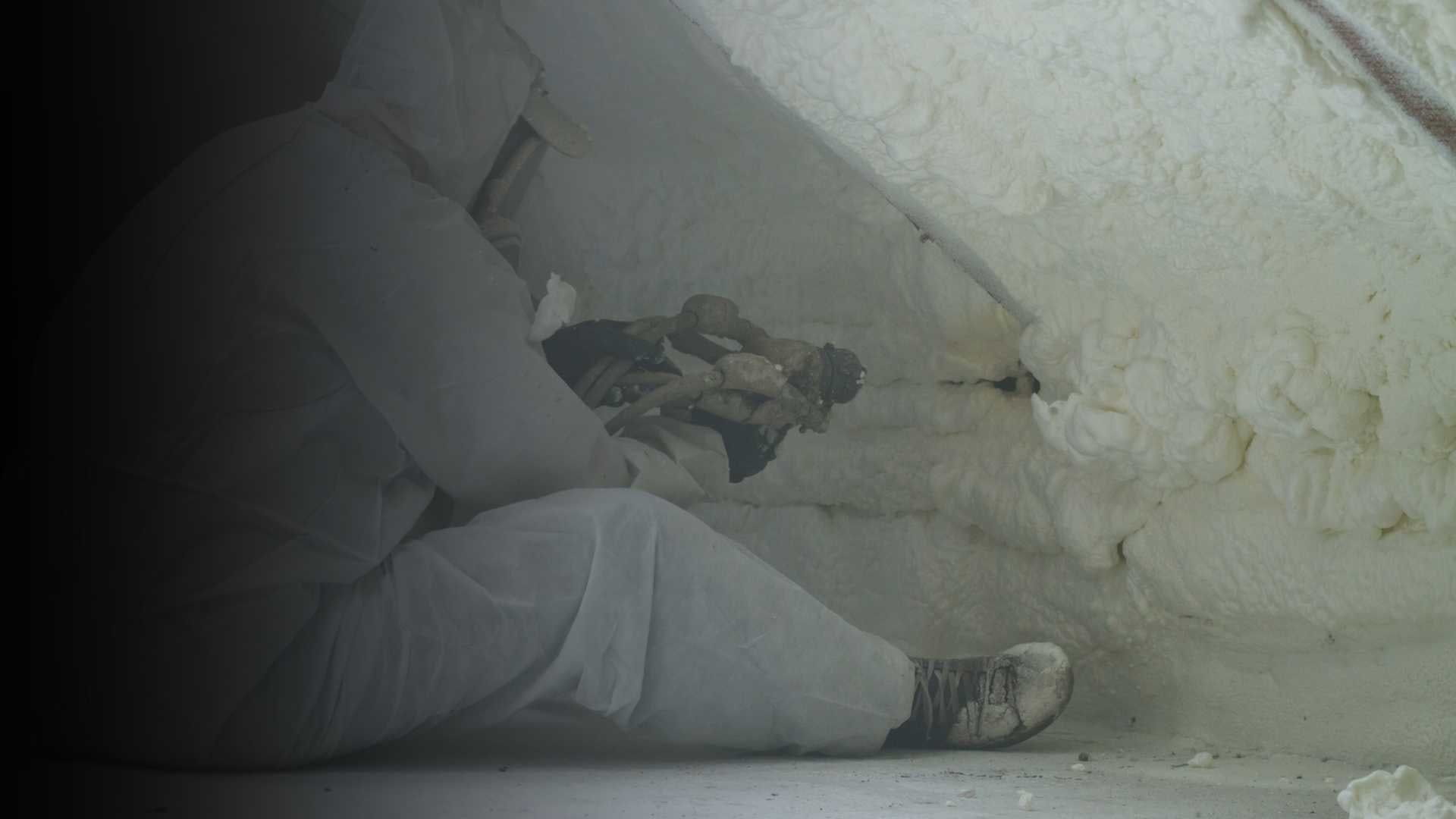 Tecnico in tuta protettiva che applica materiale isolante in un sottotetto