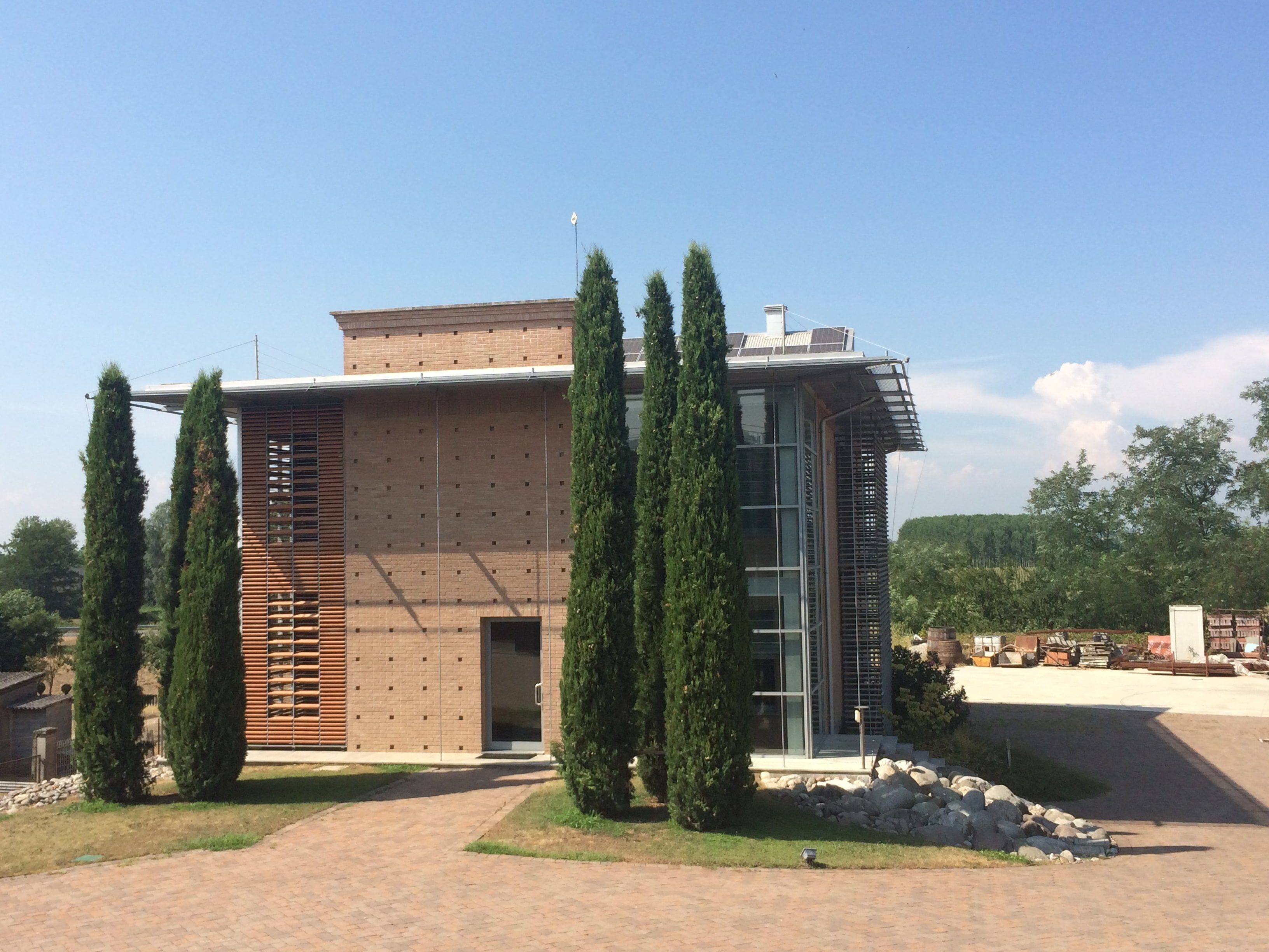 La sede di Bosio Costruzioni a San Bassano: edificio in mattoni con frangisole in legno, vetrate e cipressi